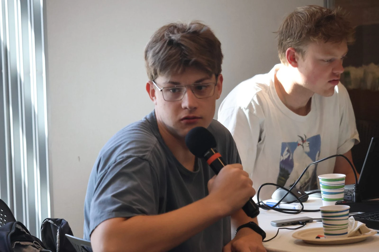 Two participants work at a table during an Evoke challenge at CU Boulder, one of them speaking into a microphone.